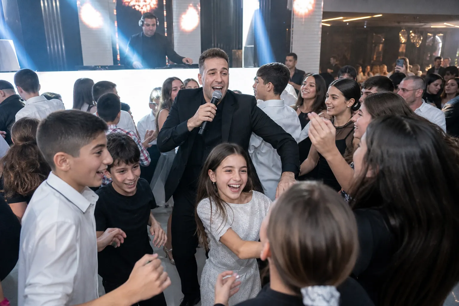 אוראל מרקוביץ׳ מוביל את הרחבה עם מיקרופון בבת מצווה, ילדים רוקדים סביבו
